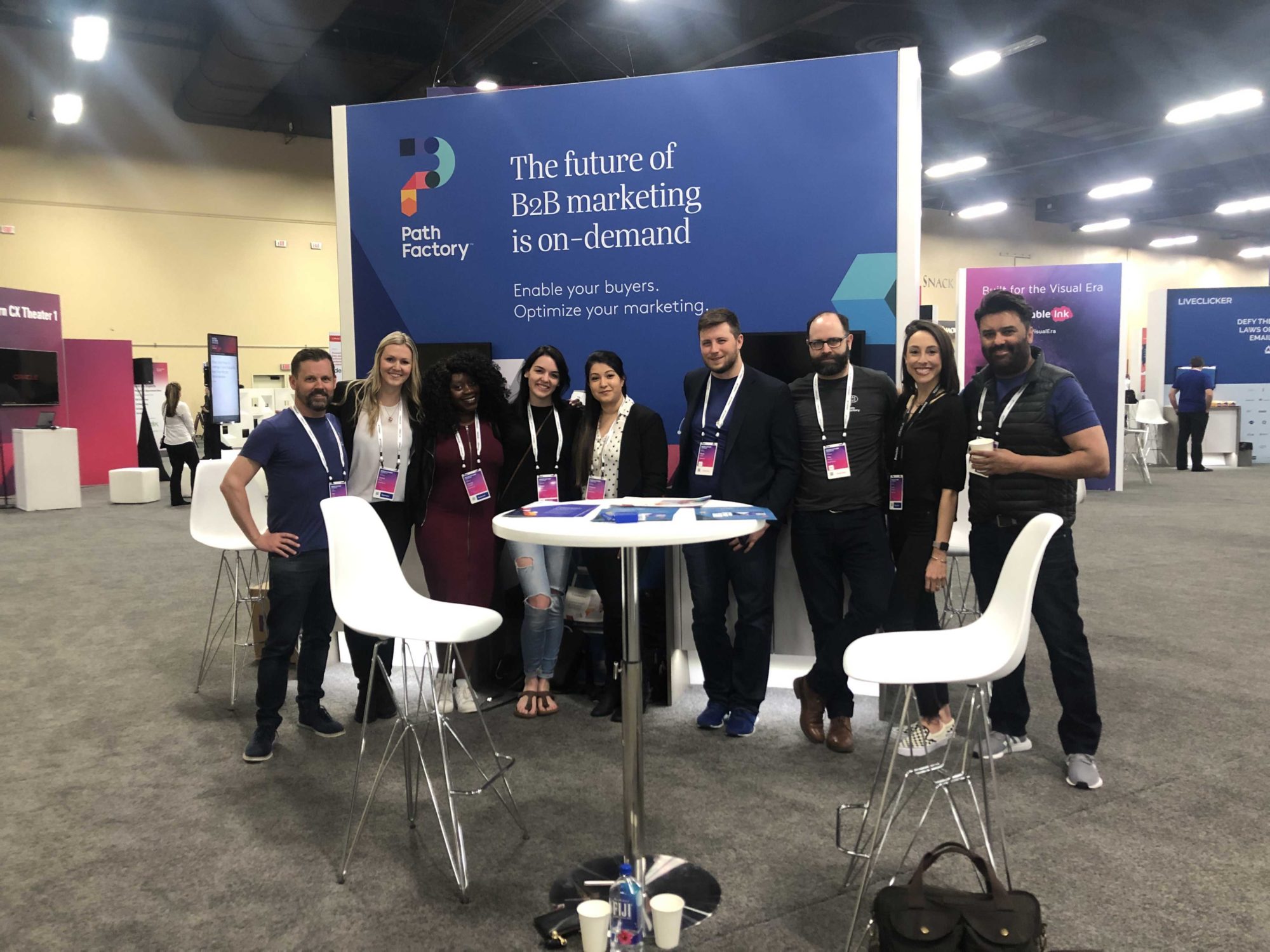 Photograph of PathFactory Employees at an Event with a sign in the background that says:  The future of B2B marketing is on-demand, Enable your buyers.  Optimize your marketing